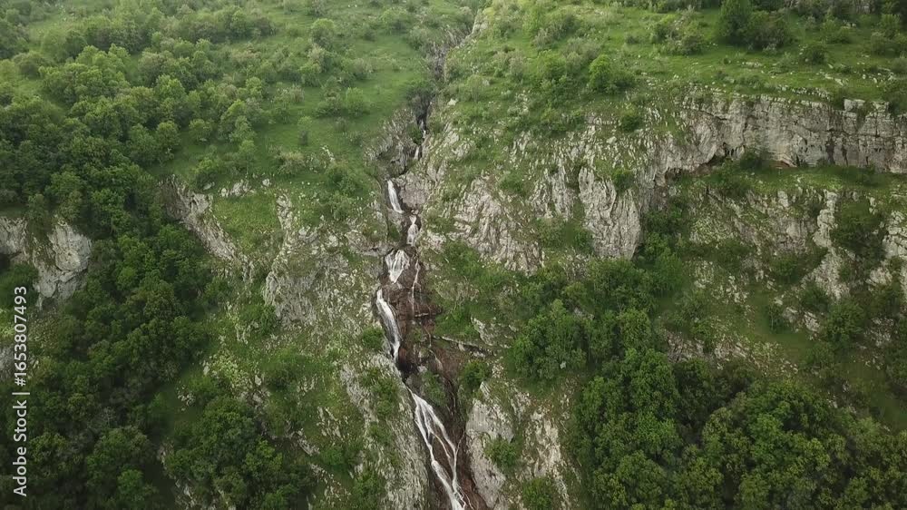 Poster aerial view of a landscape with a waterfall cascading down a rocky terrain surrounded by trees and g