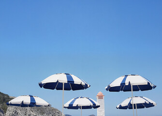 A series of blue and white striped umbrellas arranged on a white stone wall against a clear blue sky.