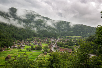 Fototapeta premium Traditional Shirakawa-go village in summer rain with rice fields and misty mountains