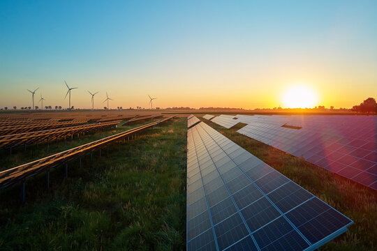 Rows of solar panels and wind turbines in countryside field at sunset. Concept of renewable energy, sustainable technology and clean electricity production