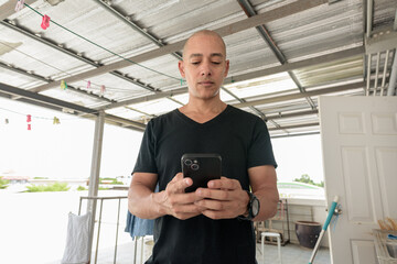 Hispanic bald man using phone while doing laundry outdoors during day