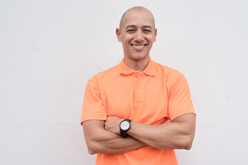 Bald Italian man in orange polo shirt studio portrait against white wall with arms crossed smiling