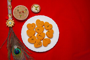 Heart Shaped Mithai on a white Plate with a Decorative Peacock Feather and a Red Background