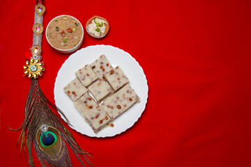 Traditional Festival Barfi Dessert on a white Plate with a Decorative Peacock Feather and a Red Background