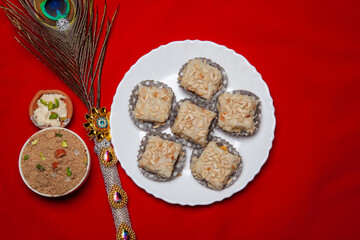 Traditional Festival Barfi Dessert on a white Plate with a Decorative Peacock Feather and a Red Background