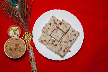 Traditional Festival Barfi Dessert on a white Plate with a Decorative Peacock Feather and a Red...