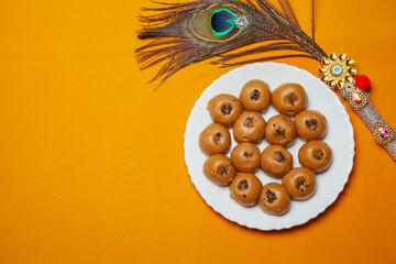 Traditional Indian Sweets Peda Mithai on White Plate with Decorative Peacock Feather on Yellow Background