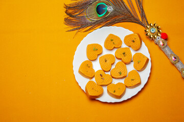 Heart Shaped Mithai on a white Plate with a Decorative Peacock Feather and a Yellow Background