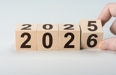 Male hand turning wooden cube to reveal year 2026, leaving 2025 behind. New beginnings and fresh...