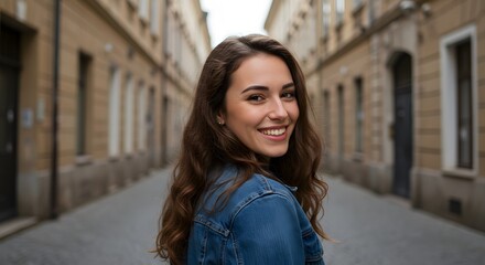 Fototapeta premium Young woman smiling in a denim jacket on a cobblestone street in an old european town