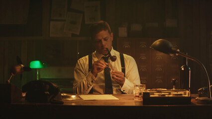 Journalist smoking pipe and preparing tobacco in his office at night