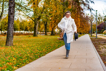 Beautiful mature woman walking in city park on autumn day. Front view