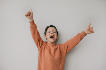 A preschool boy on a light background shows a thumbs up