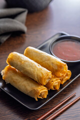 Fried spring rolls and sweet and sour sauce on wooden table.