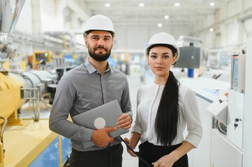 Engineers holding laptop and tablet, supervising production line in factory