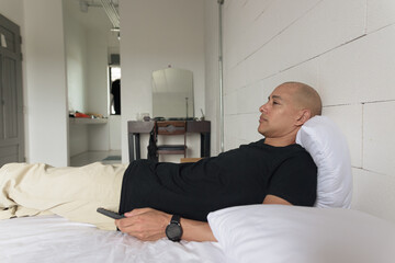 Man lying down on bed and watching television at home