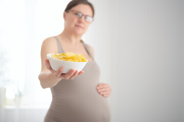 Close-up of future mother snacking on potato chips while stroking her baby bump. Honest portrayal...