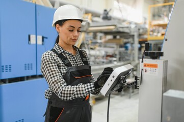 Female factory worker operating machinery using digital tablet in modern industrial setting