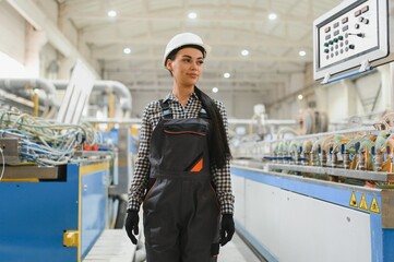Female factory worker wearing hardhat supervising production line in modern industrial facility