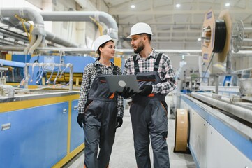 Engineers walking and discussing production with laptop in factory