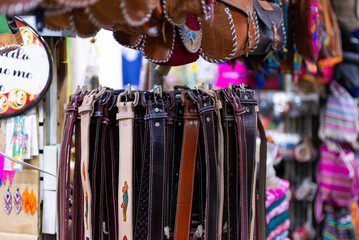 A vibrant display of handcrafted leather belts in various colors and styles hangs in a market