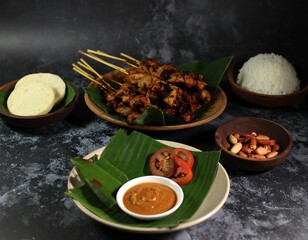 Authentic Indonesian satay platter featuring grilled chicken skewers with peanut sauce, rice, and traditional side dishes on banana leaves