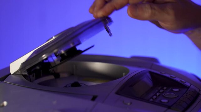 A close-up of a hand inserting a compact disc CD into the open tray of an old or vintage portable CD player
