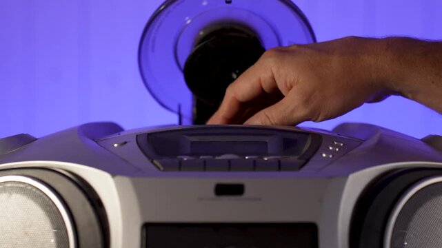 A close-up of a hand inserting a compact disc CD into the open tray of an old or vintage portable CD player