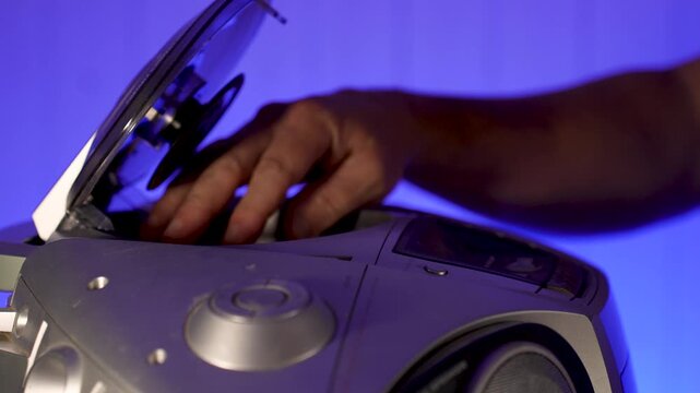 A close-up of a hand inserting a compact disc CD into the open tray of an old or vintage portable CD player