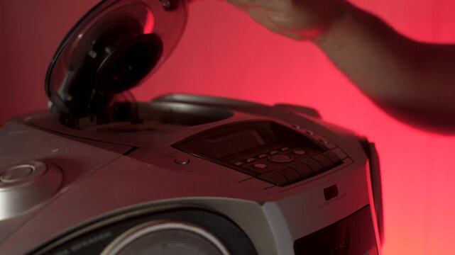 A close-up of a hand inserting a compact disc CD into the open tray of an old or vintage portable CD player