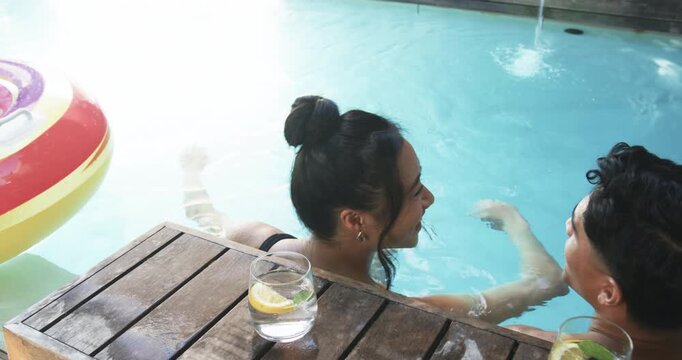 Relaxing diverse couple leaning on deck at pool, with lemon water glasses, beach ball - Powered by Adobe