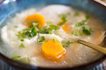 Broth with dumplings, carrots and parsley in a decorative bowl.
