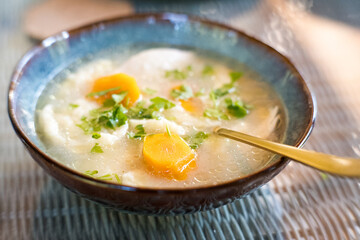 Broth with dumplings, carrots and parsley in a decorative bowl.
