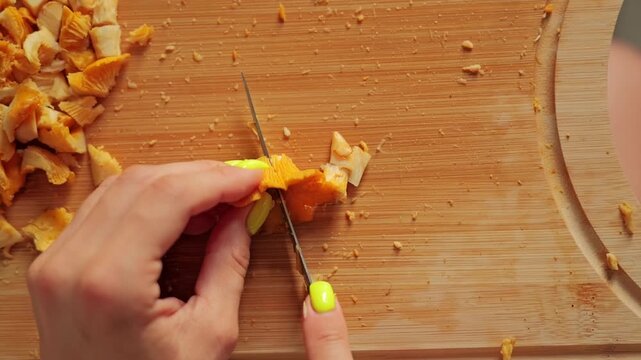 Macro top down view of chanterelles being chopped into small pieces, wood board