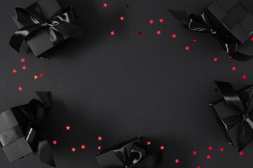 Stylish black gift boxes decorated with satin ribbons and red confetti on a black background are...