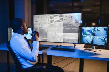 African American security officer or dispatch uses computer and walkie talkie, looks at screens