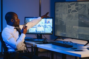 African American security officer or dispatch uses computer and walkie talkie, looks at screens