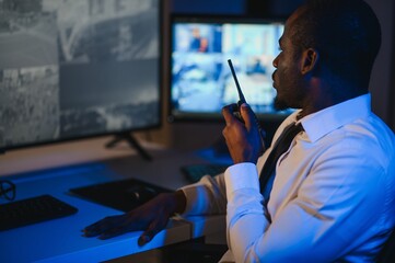 African American security officer or dispatch uses computer and walkie talkie, looks at screens