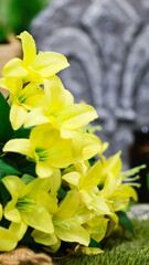 Close-up of a silver fleur-de-lis pendant displayed on a stone relief with carved lily symbol, surrounded by colorful spring flowers. Represents medieval heritage, tradition and cultural symbolism