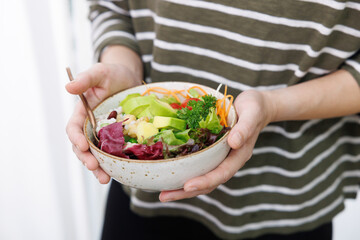 A person holds a fresh and healthy salad bowl with two hands. The perfect concept for a nutritious,...