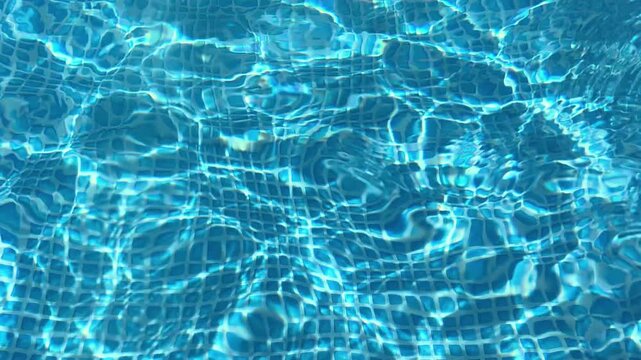 Crystal-clear water ripples gently in a swimming pool, its surface reflecting sunlight and revealing the blue mosaic tiles below, creating a mesmerizing and refreshing summer scene.