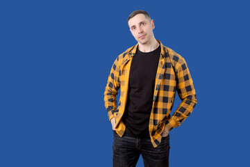 A man in a plaid shirt and black pants stands in front of a blue background. Isolated portrait of a...