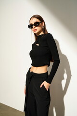 Stylish young woman in black outfit posing with sunglasses.