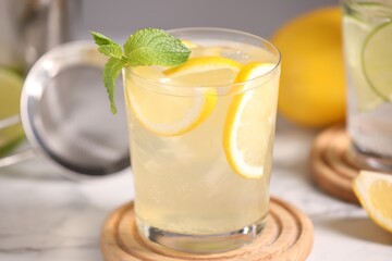 Tasty cocktail with lemon slices and mint in glass on white table, closeup
