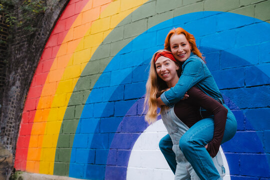 Happy friends posing playfully in front of colorful rainbow mural outdoors