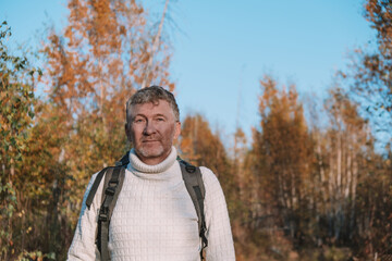 Obraz premium man is hiking through serene forest filled with autumn foliage. he wears cozy sweater and carries backpack while enjoying nature beauty under bright blue sky. close up.