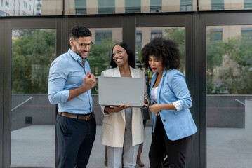 Happy multiethnic business team working on laptop outdoors in modern city setting