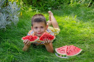 Happy child eating watermelon outdoors in summer grass