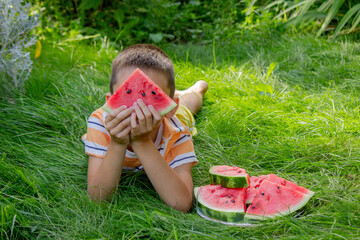 Happy child eating watermelon outdoors in summer grass