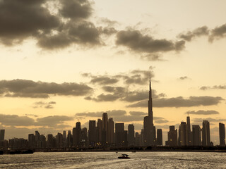 Obraz premium Cinematic Dubai skyline at sunset with golden sky and water ripples, panoramic view from Creek Harbour